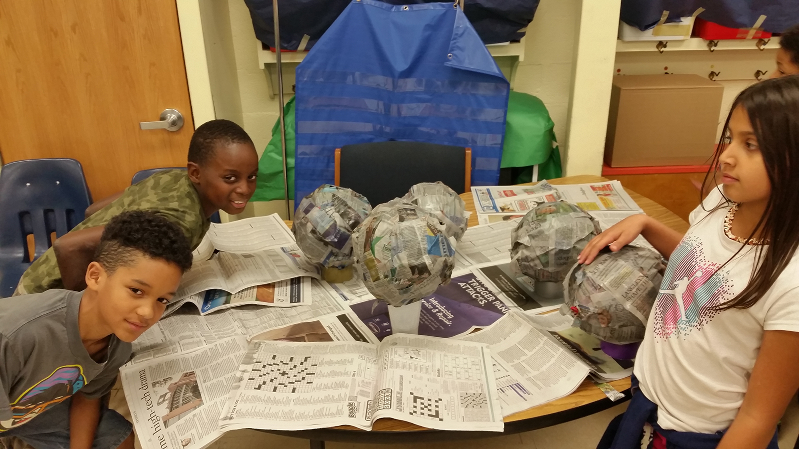 three kids in a classroom and an art project